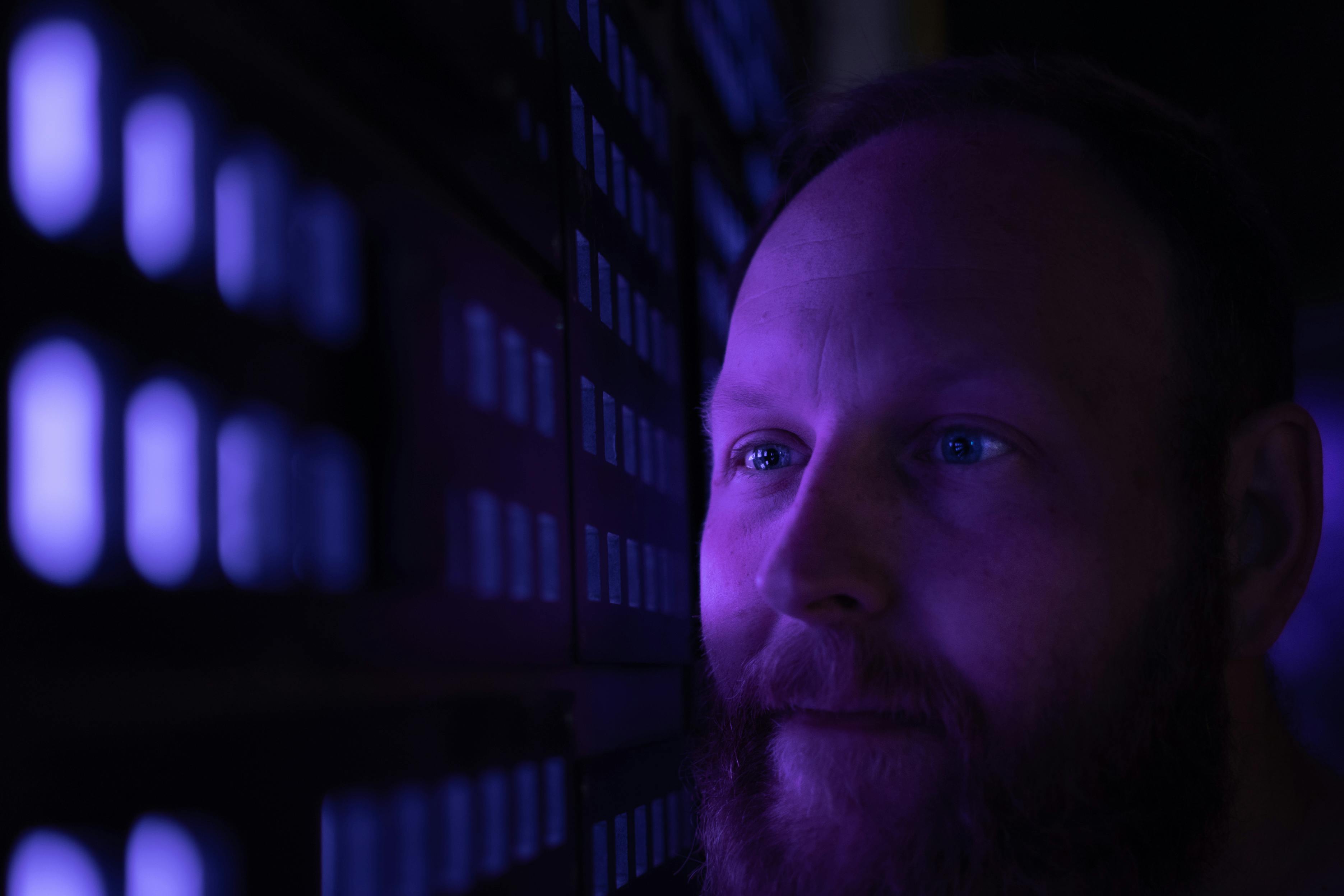 Close-up of a bearded man looking contemplatively at a purple-lit wall.