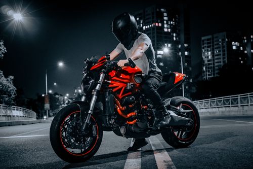 Free A biker on a red Ducati motorcycle rides through an illuminated city street at night. Stock Photo