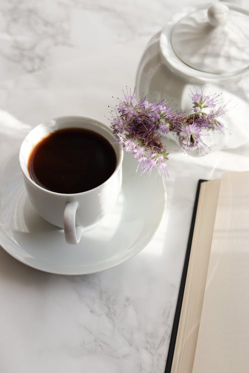 Aromatic freshly brewed black coffee served in white ceramic cup standing on table next to opened notebook and sugar bowl