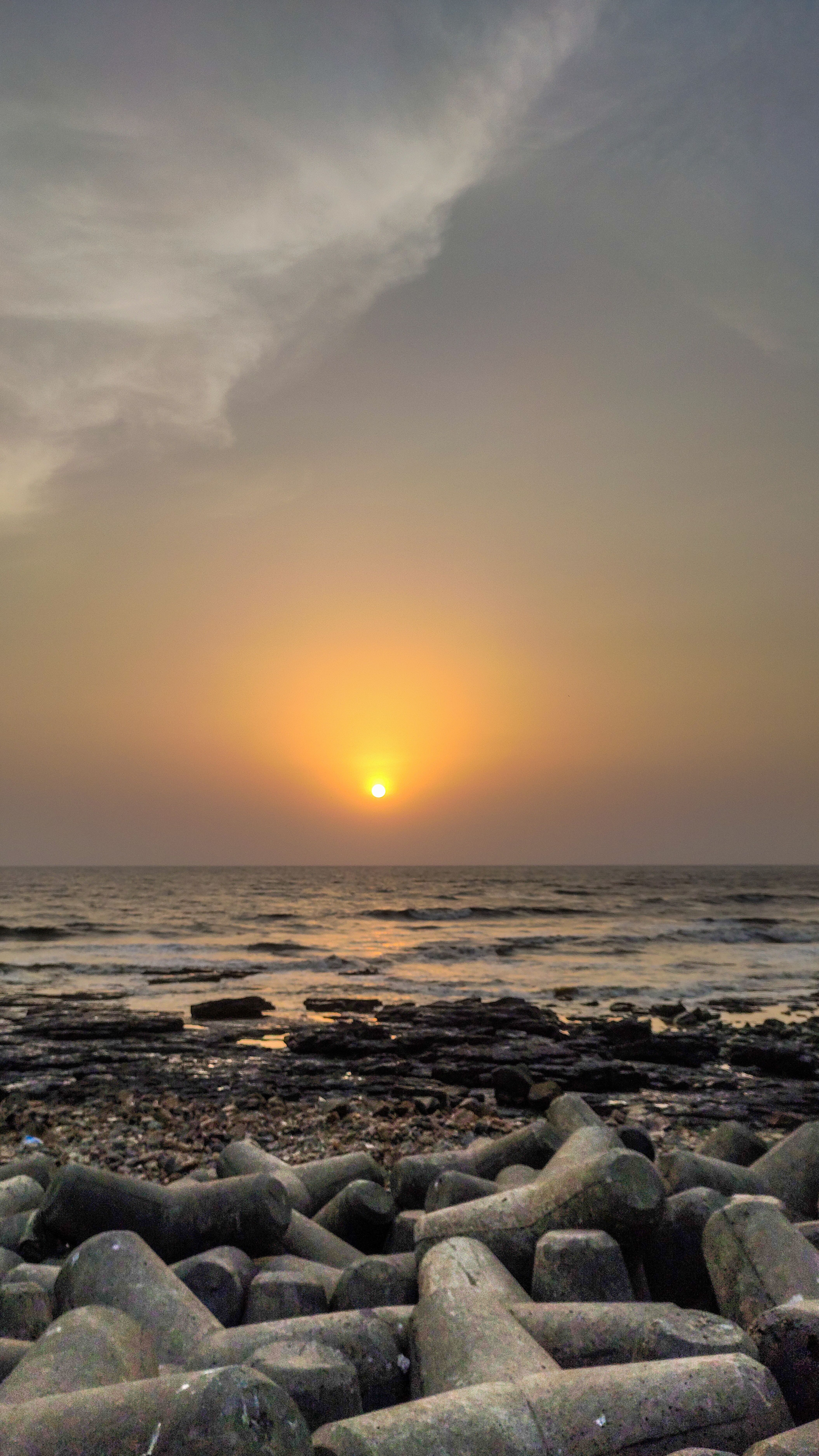 Dramatic sunset casting warm hues over a rocky seashore, evoking tranquility.