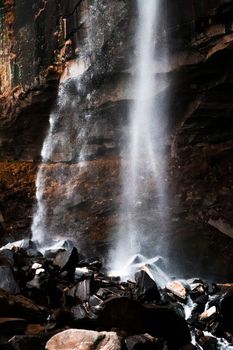 A mesmerizing vertical shot of a waterfall cascading over rocky cliffs. Perfect for nature lovers.