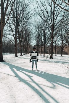 A man stands in a snowy park surrounded by bare trees, wearing winter clothing.