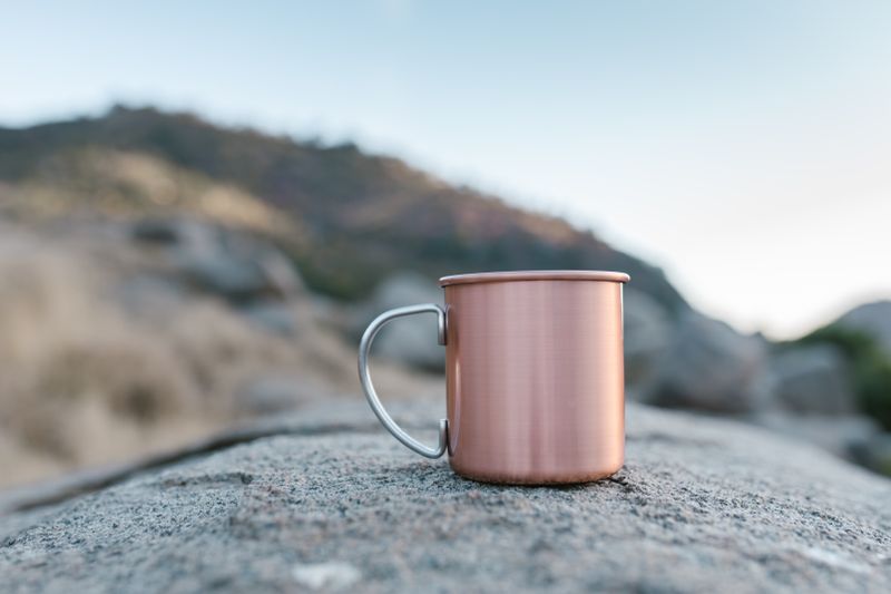 Copper mug on a rock with a blurred natural landscape in the background.