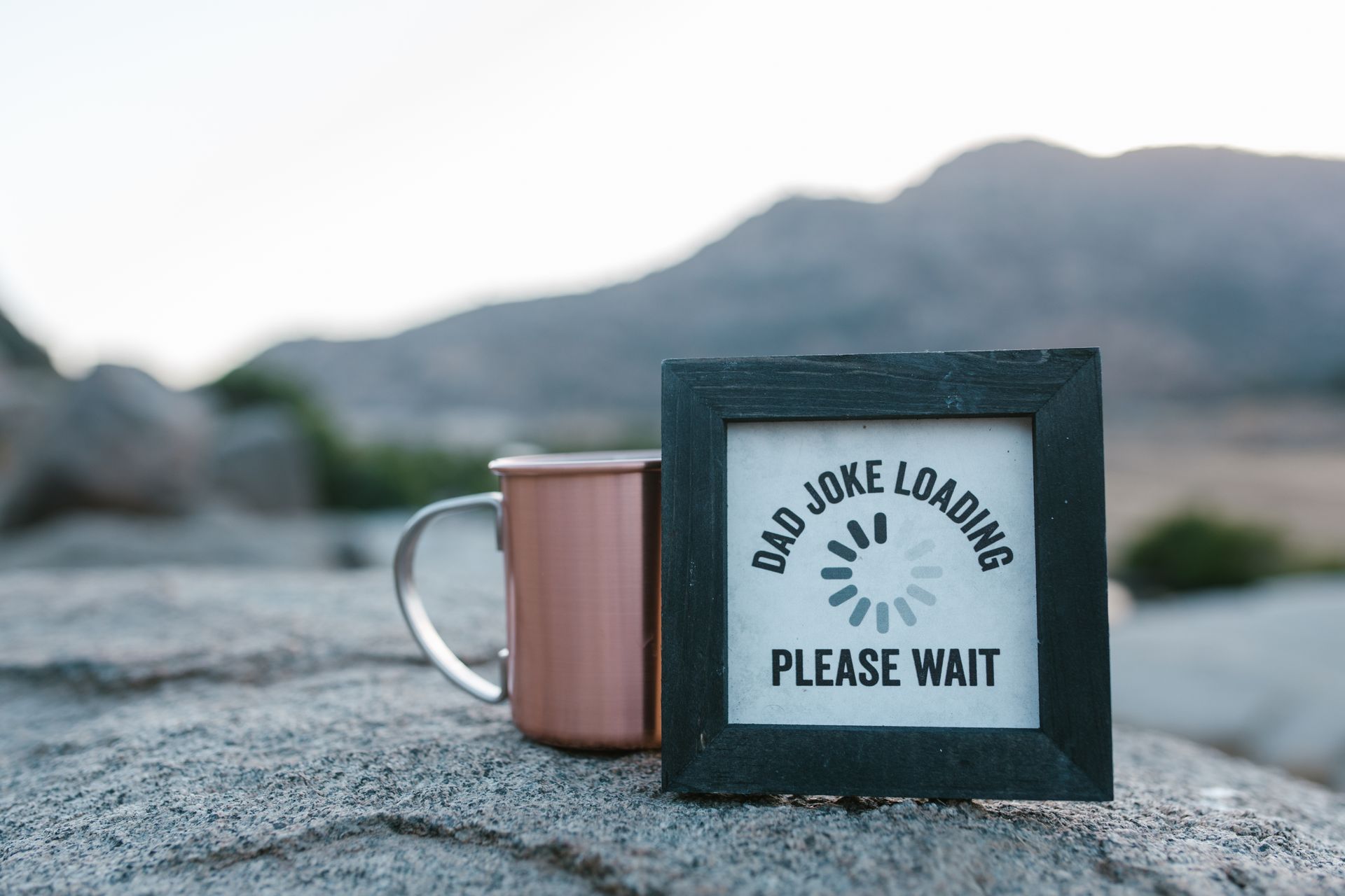 A Father's Day themed mug and wooden frame with a joke in a scenic outdoor setting.