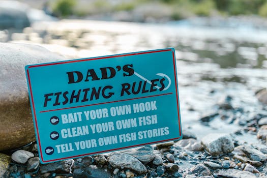 A close-up of a fun sign highlighting dad's fishing rules placed by a river, perfect for Father's Day.
