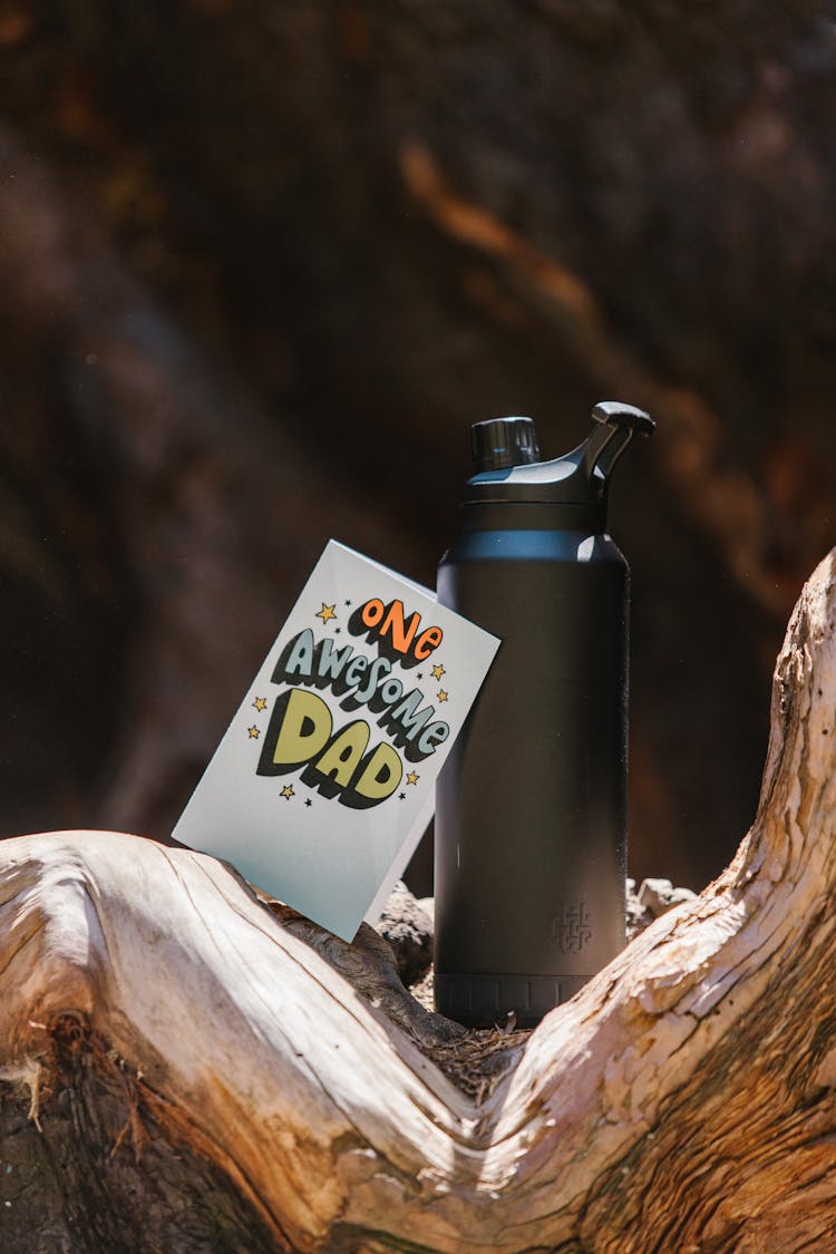 Black Water Bottle And A Card On A Tree Trunk