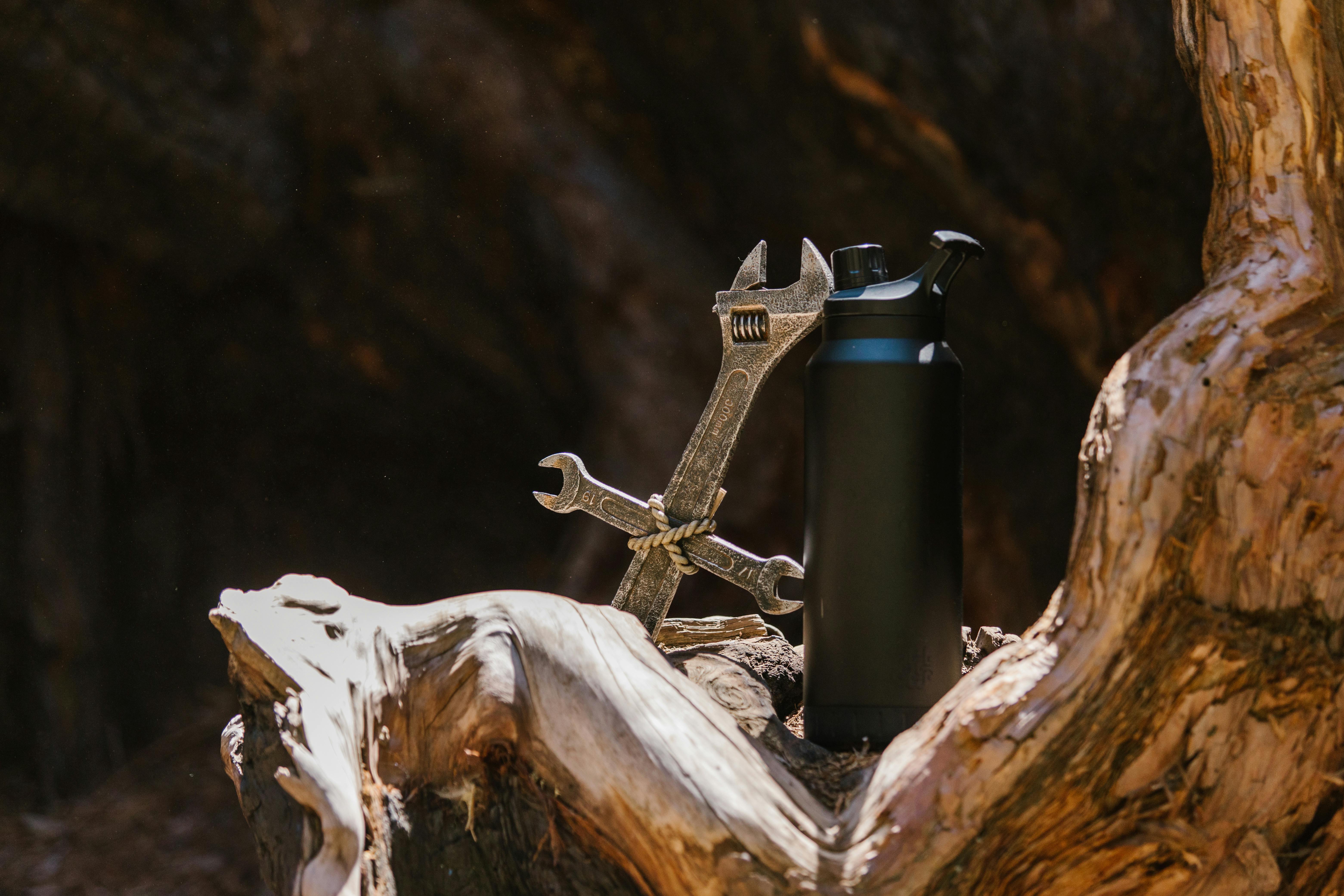 Creative arrangement of a thermos and wrenches on a tree trunk in natural light. guide