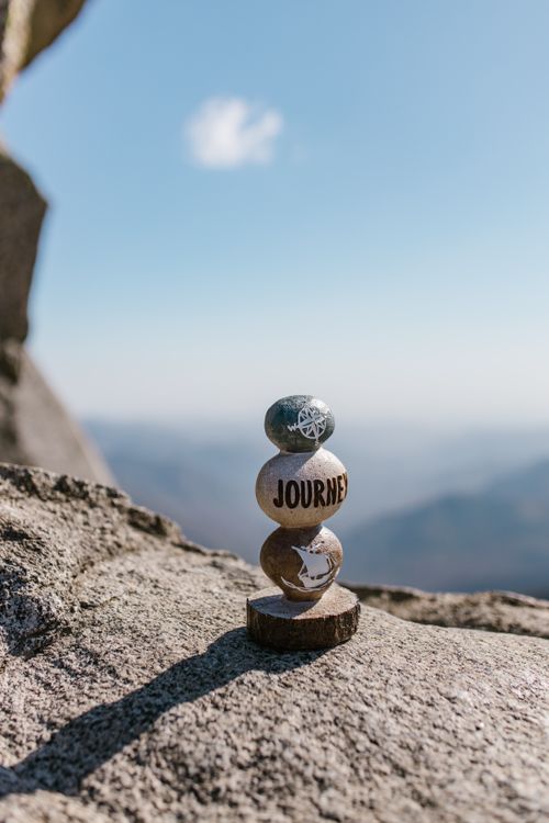 Free A stack of rocks with 'Journey' engraved, set against a serene mountain backdrop. Stock Photo