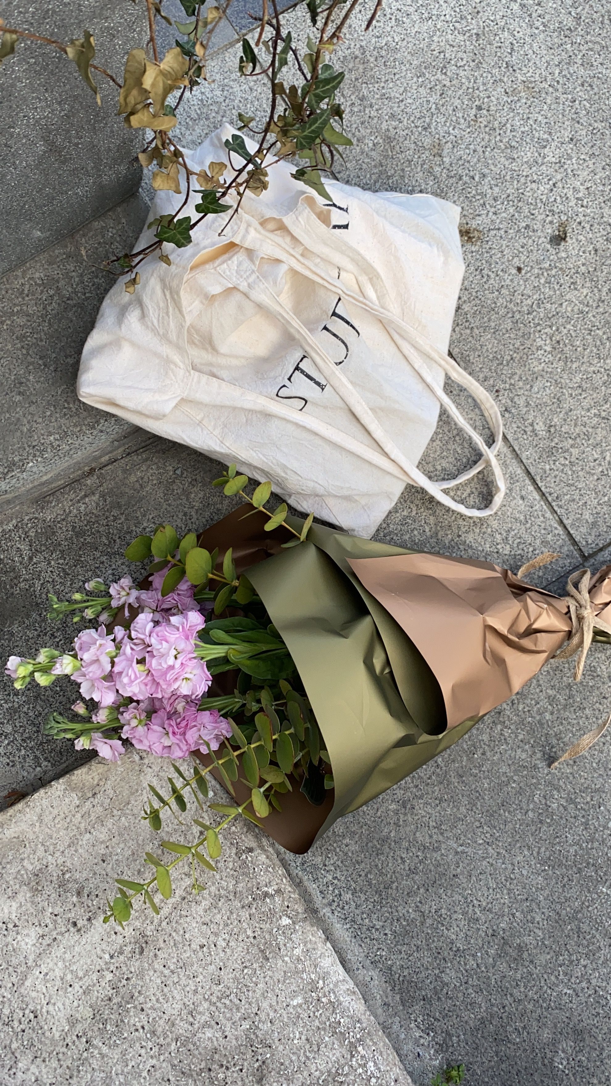 A stylish arrangement of flowers and a canvas bag on an urban sidewalk.