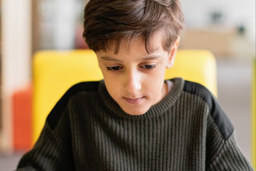 Free Young boy concentrating indoors, engaging at a table with blurred background. Stock Photo
