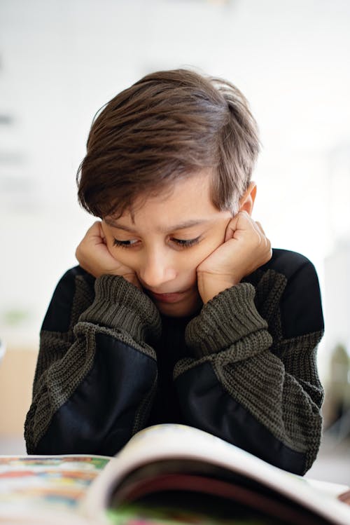 Boy in Khaki Sweater Thoughtfully Reading Book 