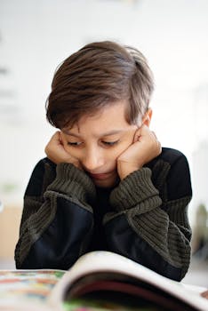 A young child in deep thought while reading a book in a classroom environment.