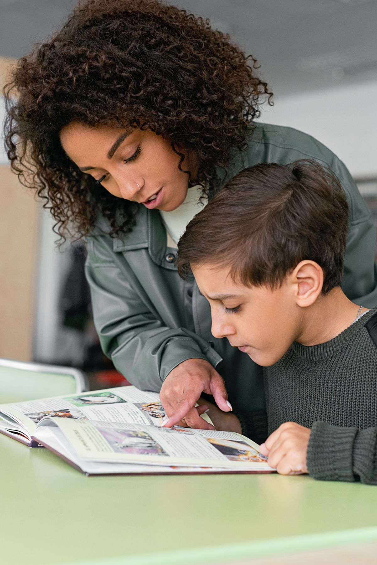 An adult and a child looking through an open book together at a table