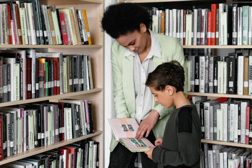 Woman Shows a Book to Boy in Library