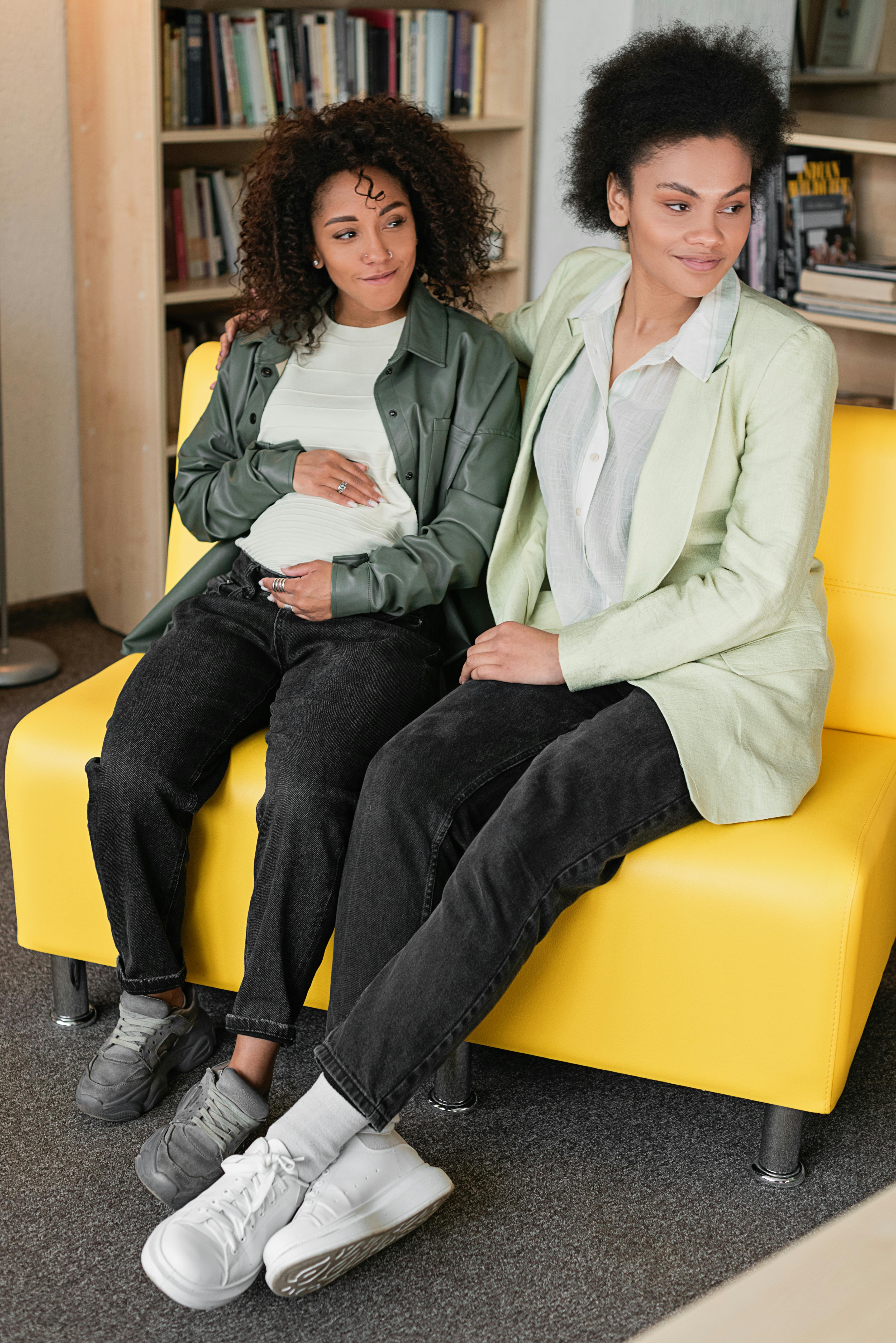 two women sitting on yellow leather couch