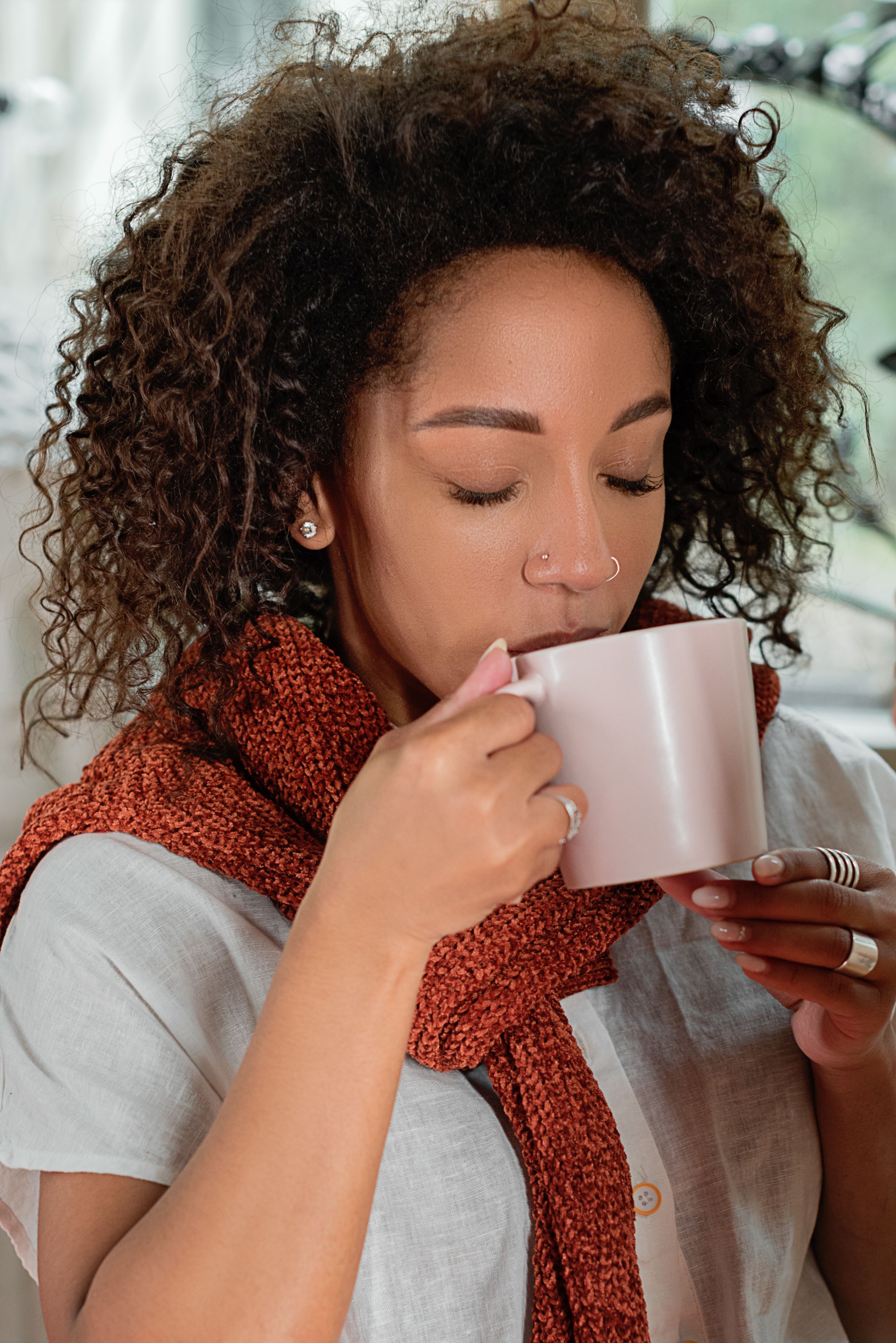 A relaxed woman enjoys a warm drink at home, wrapped in a cozy scarf.