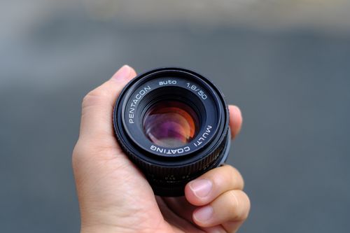 Free A clear close-up of a hand holding a camera lens against a blurred background. Stock Photo