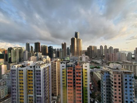 A colorful cityscape of Hong Kong's skyline with high-rise buildings under a cloudy sky.