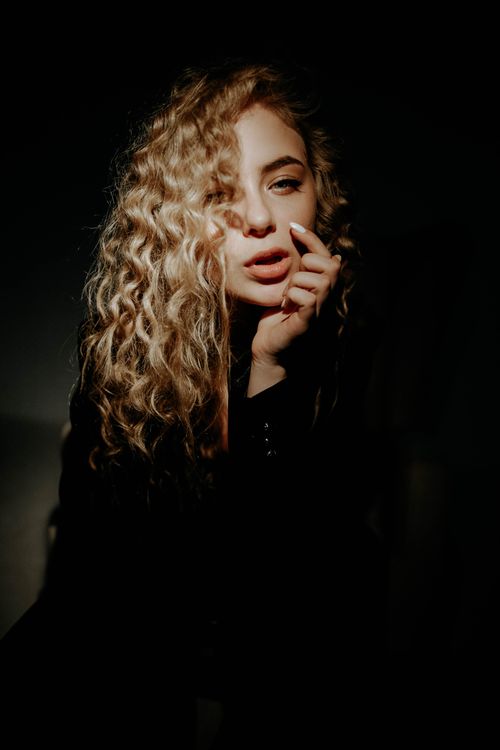 Free Captivating portrait of a woman with blonde curly hair and stylish pose in dramatic light. Stock Photo