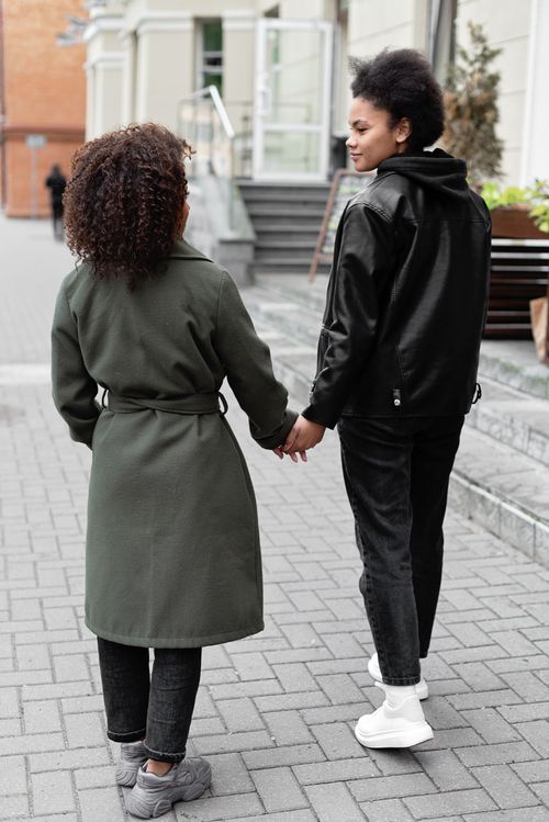 Free Two women holding hands while walking outdoors on a sidewalk, dressed in stylish jackets. Stock Photo