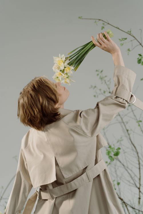 Free Elegant woman in trench coat holding a bouquet of daffodils on a neutral background. Stock Photo