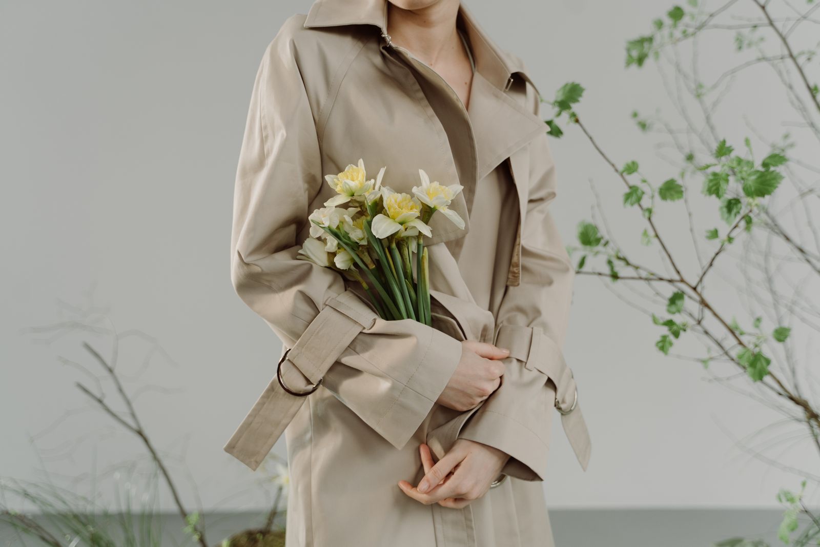 Woman in beige trench coat holding daffodils