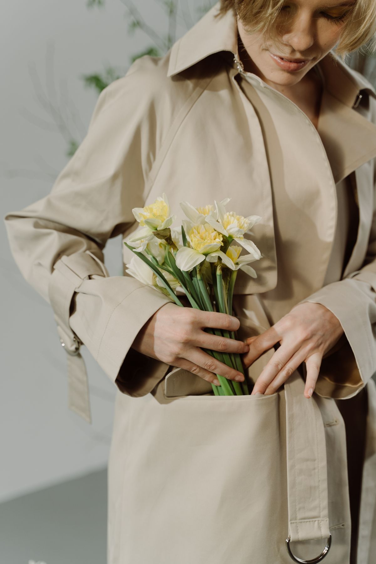 A woman in a beige coat holding white flowers — the elegant classic trench