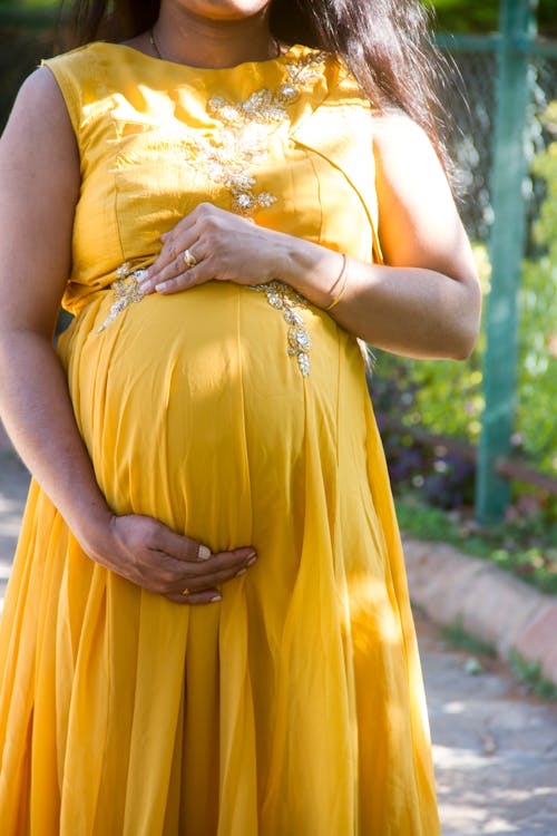 Pregnant Woman in Yellow Dress Touching Her Tummy