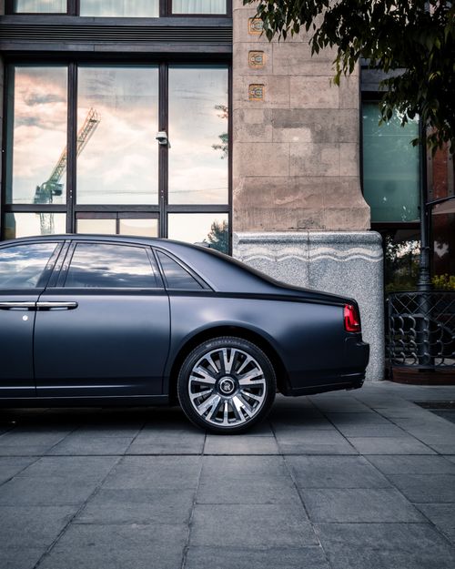 Free Sleek black luxury coupe parked beside a building with reflective windows. Stock Photo