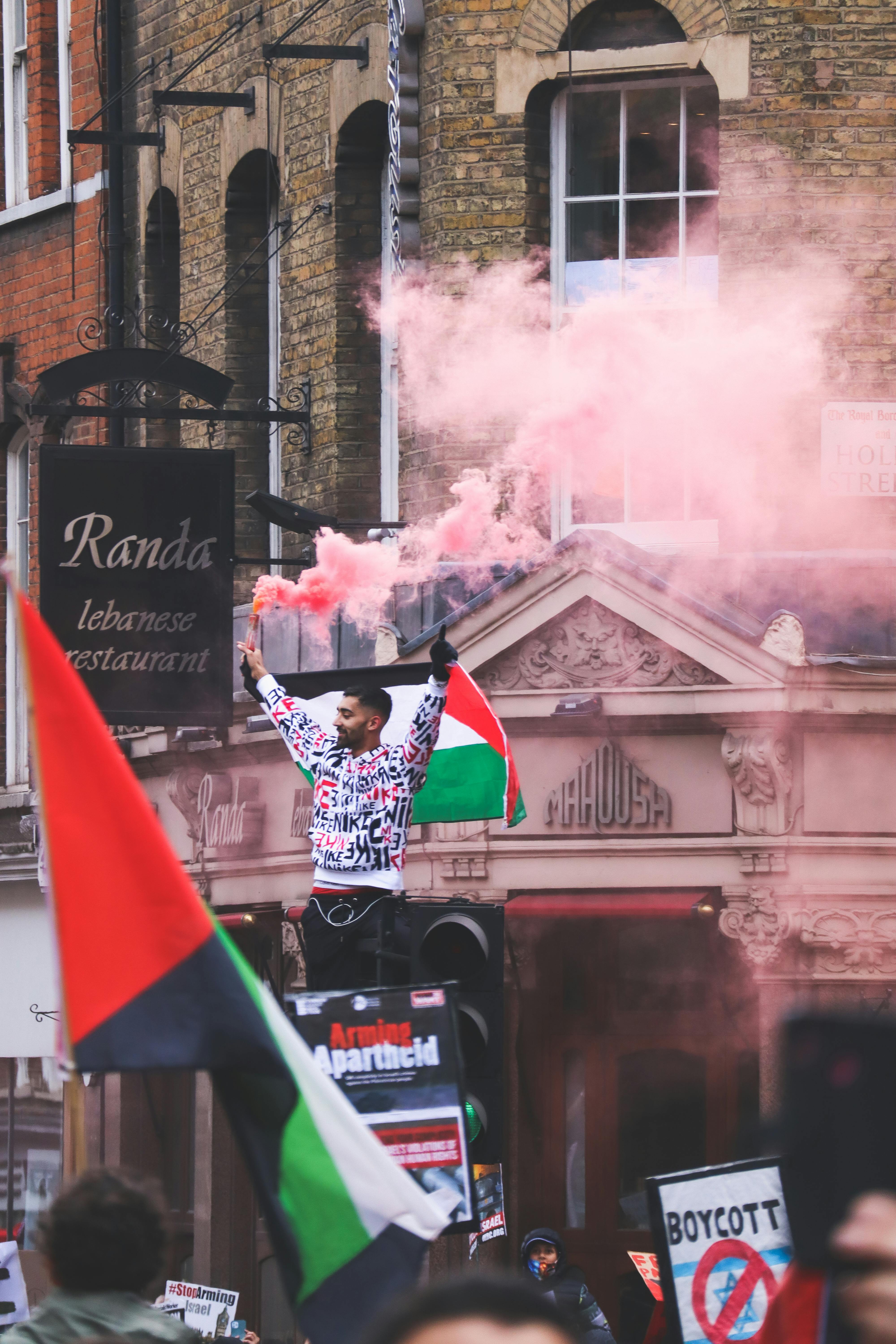 Peaceful protest with Palestinian flags and colored smoke on a bustling street.