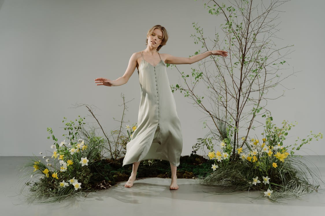 A Woman in Beige Dress Dancing beside the Plants