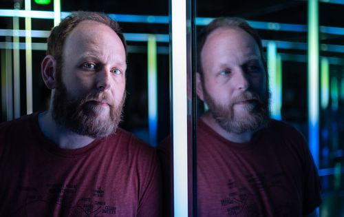 Free A thoughtful bearded man looking at his reflection in a colorful neon-lit setting. Stock Photo