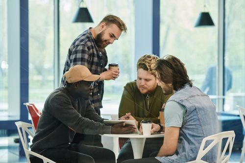 Free Four men having a collaborative meeting at a cafe, engaging with digital technology. Stock Photo