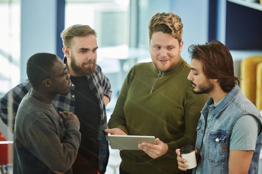 A group of four men engaging with a digital tablet in an indoor meeting setting.