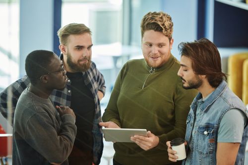 Free A group of four men engaging with a digital tablet in an indoor meeting setting. Stock Photo