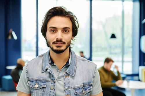 Free Relaxed portrait of a bearded man in a denim vest inside a modern cafe. Stock Photo