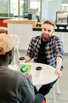 Two professionals discuss project details in a modern coffee shop.