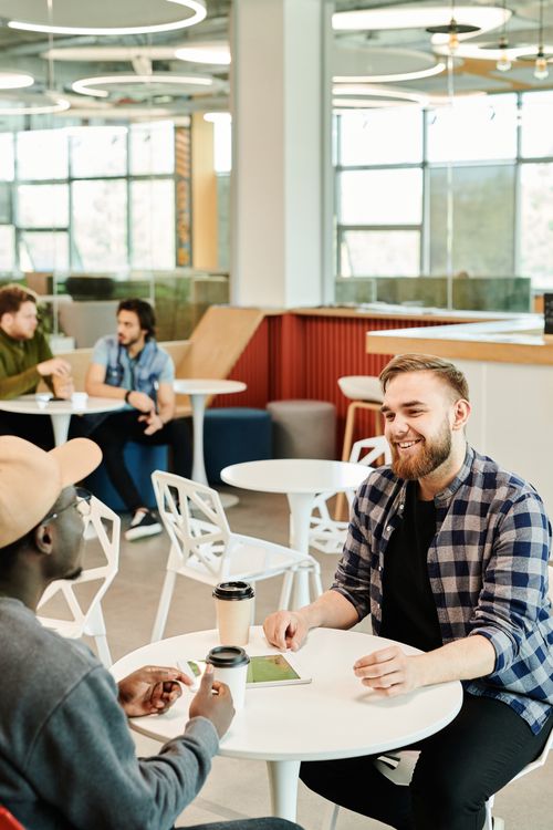 Free Colleagues engaged in conversation at a modern office cafe setting, promoting teamwork. Stock Photo