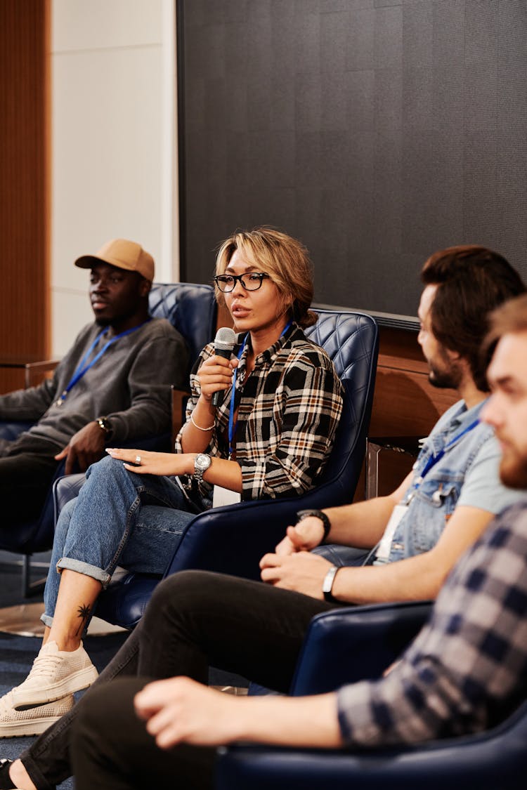 A Woman In Plaid Shirt Speaking Over A Microphone