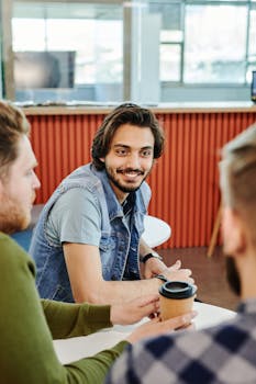 Group of young adults in a casual meeting at a modern office, smiling and enjoying coffee.