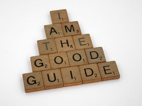 Close-up of Scrabble tiles spelling 'I am the good guide' arranged in a pyramid on a white background.