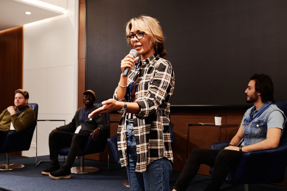 Free A confident woman speaks into a microphone during a panel discussion indoors. Stock Photo