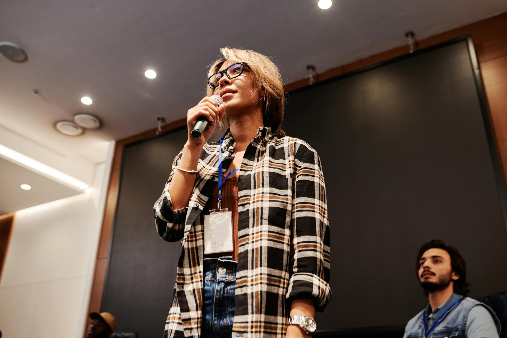 A woman speaks confidently with a microphone during an indoor presentation session.