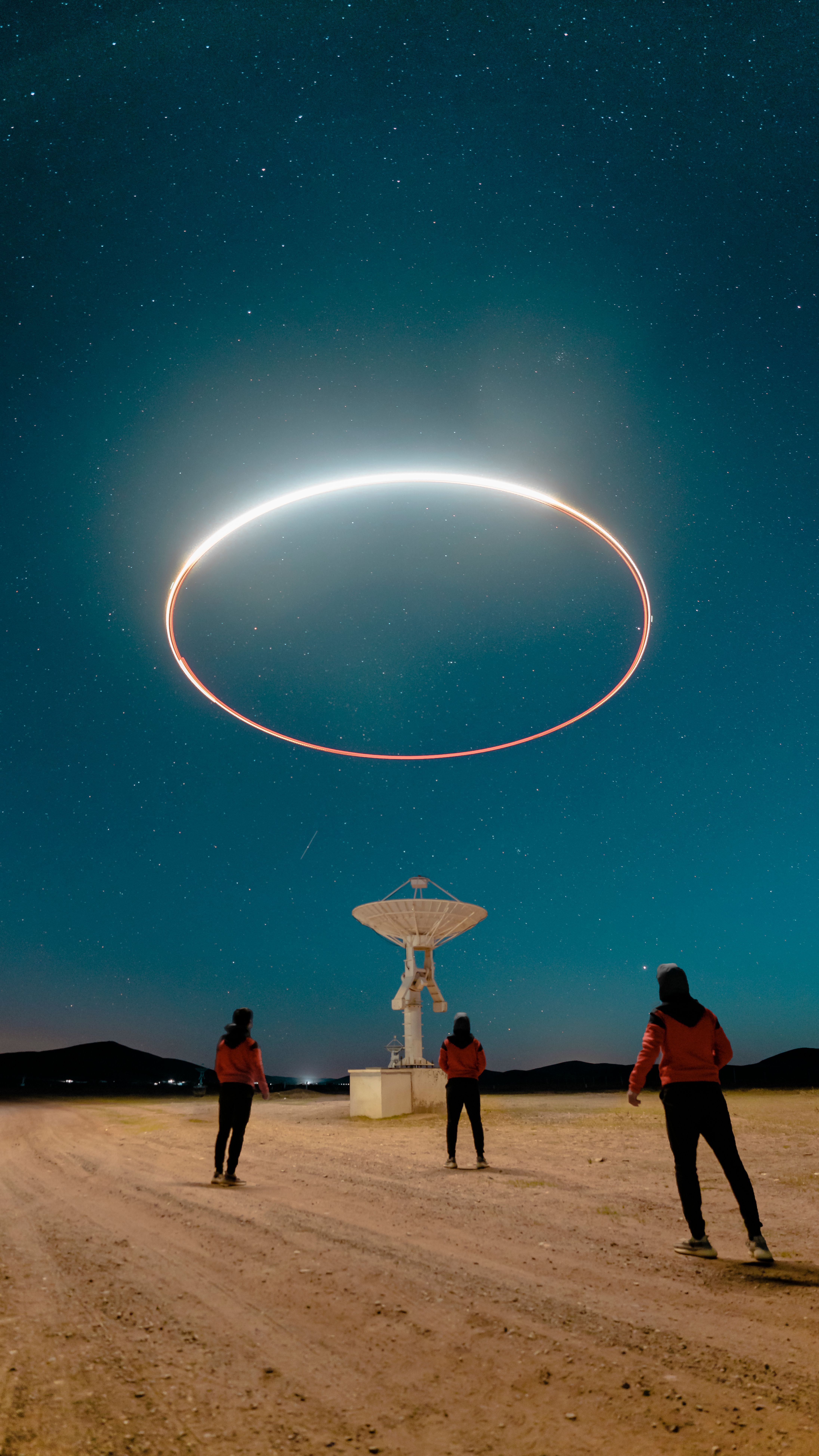 Three people observe a glowing ring above a radio telescope under a starry sky.