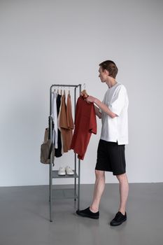 A man in casual wear selects from a stylish clothing rack in a minimalist studio setting.