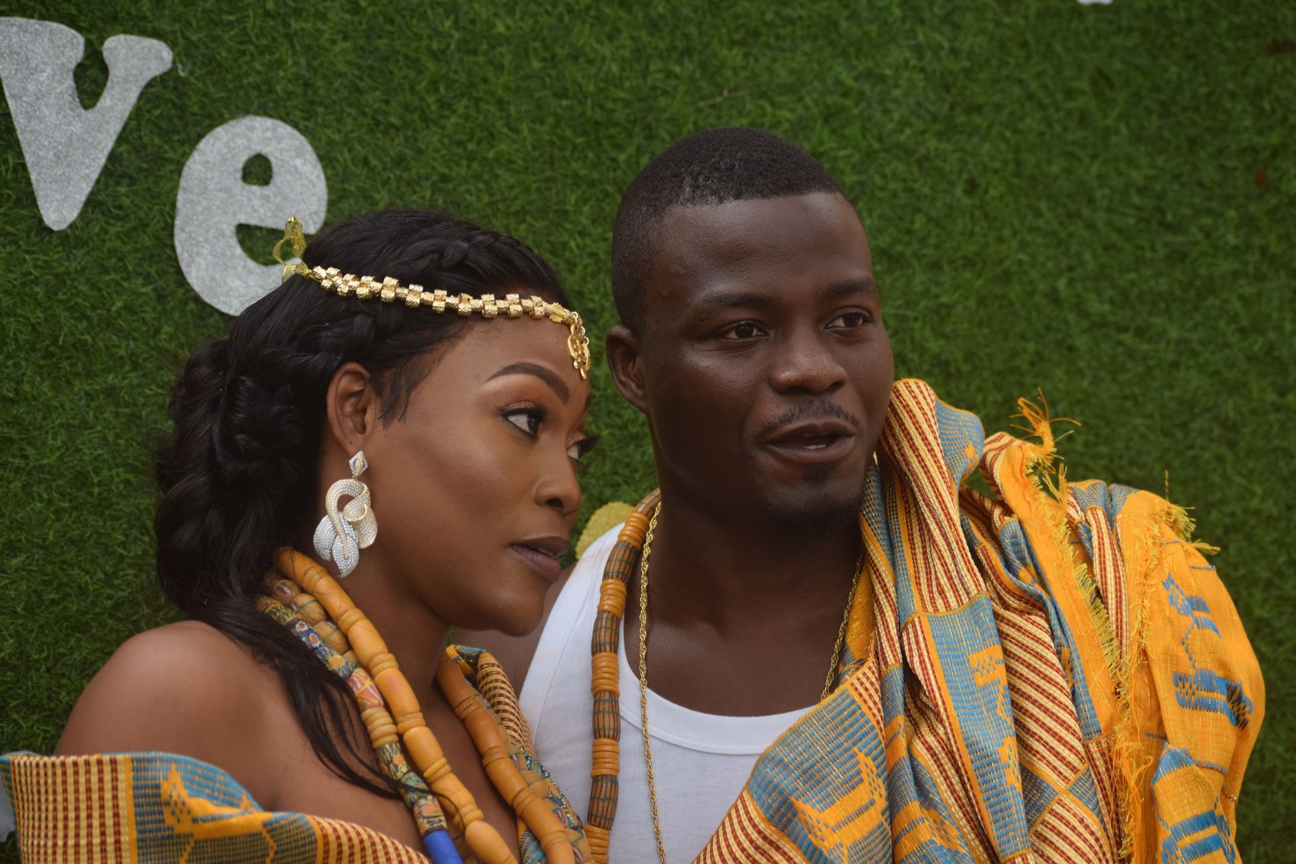 A joyful African couple wearing vibrant kente cloth and jewelry, celebrating together outdoors.