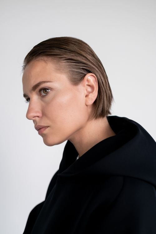 Free Moody portrait of woman in a black hoodie looking sideways against a neutral background. Stock Photo