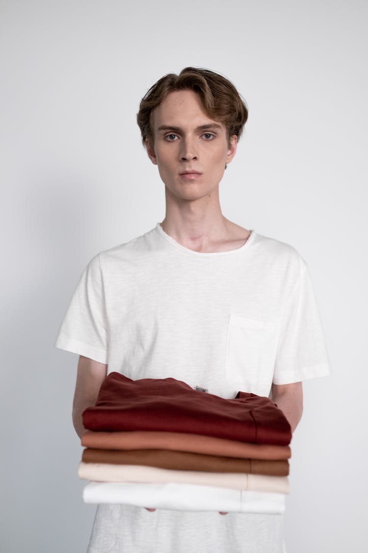 A Person In White Shirt Holding A Stack Of Clothes