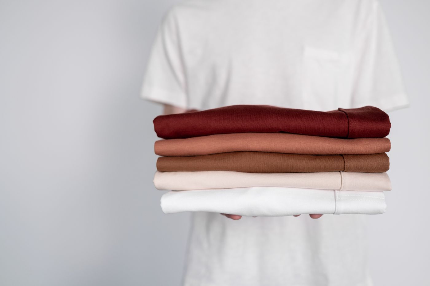 Person holding a stack of neatly folded shirts in earthy tones