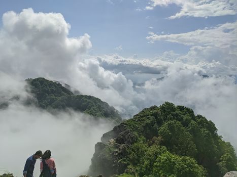 Two people embrace on a misty mountain with lush greenery and foggy vistas.